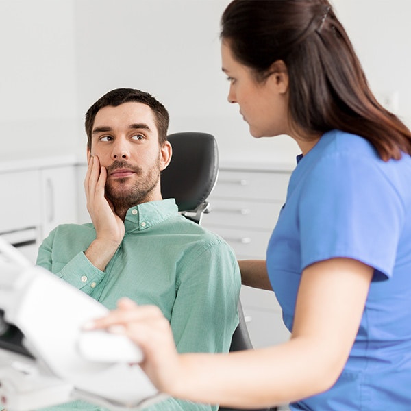 Man holding cheek in dental chair